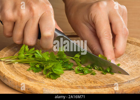 hands of woman chopping parsley leaves on the wooden cutting board Stock Photo