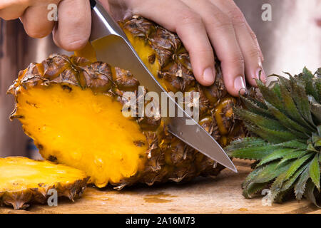 hands cutting pineapple on a cutting board, closeup Stock Photo