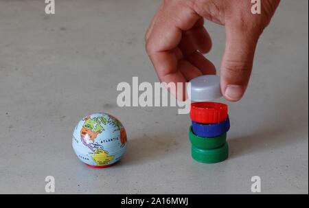 Small earth globe next to hand stacking pet bottle caps representing plastic pollution and the need for recycling. Stock Photo