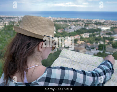 Pretty young brunette woman with a map of a village stands on a mountain, looks at a map, studies a travel route Stock Photo