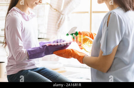 Girl wearing rubber gloves and helping mother to clean flat Stock Photo