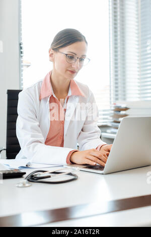 Doctor doing paperwork on computer sitting on desk Stock Photo