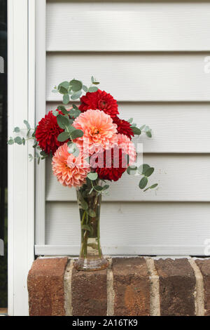 Vase Full of Dahlia Flowers and Eucalyptus Greens In Front of White Siding Background Stock Photo