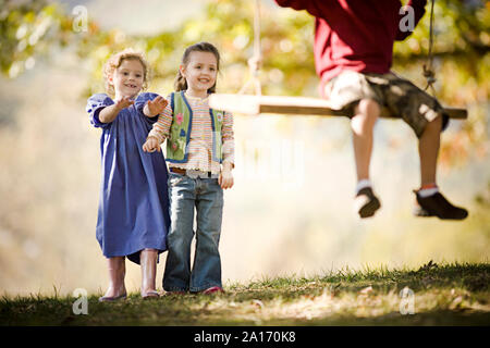 Girls pushing boy on a swing Stock Photo