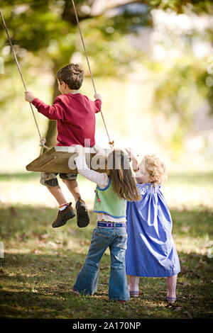 Girls pushing boy on a swing Stock Photo