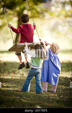 Girls pushing boy on a swing Stock Photo