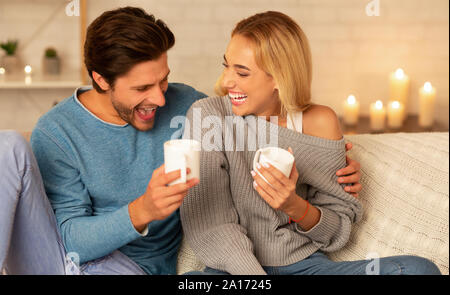 Couple Laughing Sitting On Couch Drinking Coffee Indoor Stock Photo