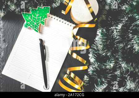 A white notebook with a black pen lies on the table next to Christmas tree decorations Stock Photo