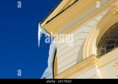 Part of Building with Icicles and Snow Against Blue Sky in Switzerland. Stock Photo