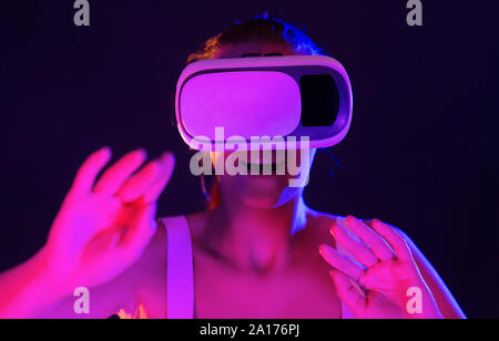 Excited woman using VR headset, touching air in colorful lights Stock Photo