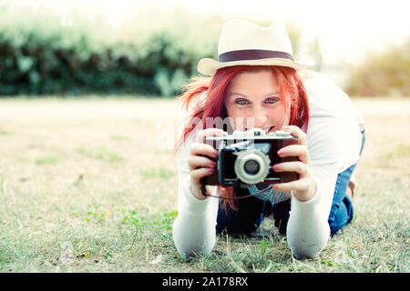 Portrait in the nature of a beautiful smiling red-haired woman using an old camera. vintage treatment Stock Photo