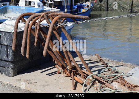 Rusty anchors propped up against wall on harbour sea and boat in background Stock Photo