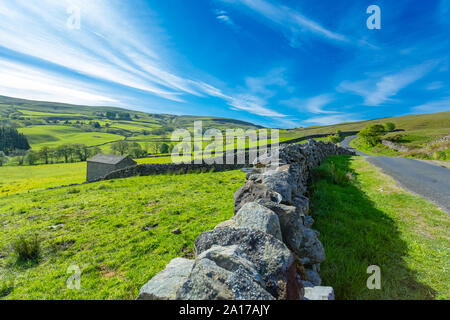 Yorkshire Dales scenic landscape.  Single track road from Askrigg to Gunnerside and Muker.  Blue sky, drystone walling and green fields. Landscape