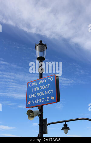 A sign stating 'Give Way to Lifeboat Emergency Vehicle', with a blue sky and cloud background, at the end of Southend Pier. Stock Photo