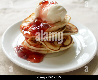 Fresh hot pancakes stack with strawberry jam and sour cream on white plate on natural light linen tablecloth background. Soft focus. Copy space. Panca Stock Photo