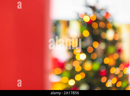 Defocused Christmas tree with bokeh lights seen through red open door. Christmas frame. Xmas blur background. Christmas banner with negative space. Stock Photo