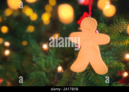 Christmas concept with a gingerbread man hanging in a green Christmas tree decorated with Xmas string lights. Christmas traditional tree close-up. Stock Photo