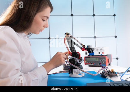 A young woman writes an algorithm for the robot arm. Science Research Laboratory for Robotic Arm Model. Computer Laboratory Stock Photo