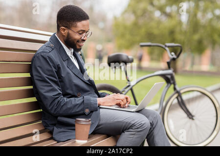 Freelancer working on laptop in park on bench Stock Photo