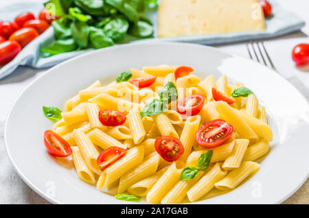 Colorful penne rigate pasta dish with cherry tomatoes and basil leaves. Stock Photo