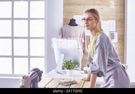 Attractive fashion designer working in office, leaning on desk, drawing. Stock Photo