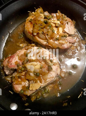 Two pork chops in a frying pan with onions, garlic, rosemary, capers and a red wine sauce Stock Photo