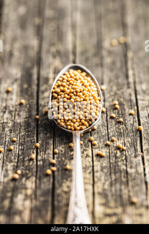 Yellow mustard seeds in spoon on old wooden table. Stock Photo