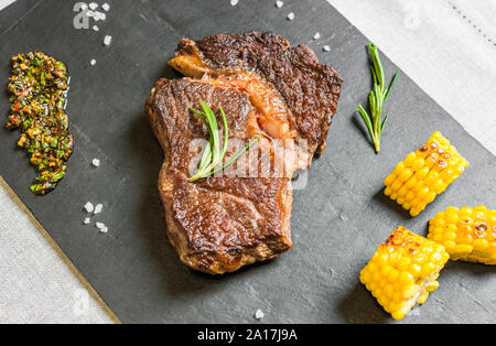 Grilled rib eye beef steak meat with chimichurri sauce against black background Stock Photo