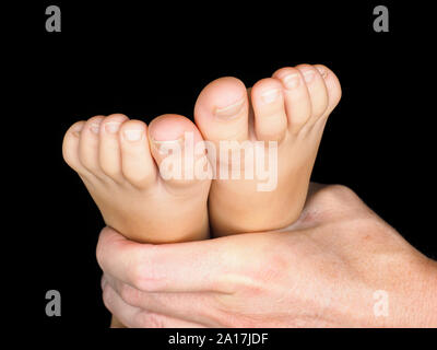 Feet of caucasian child in hand of dertmatologist doctor isolated towards black Stock Photo