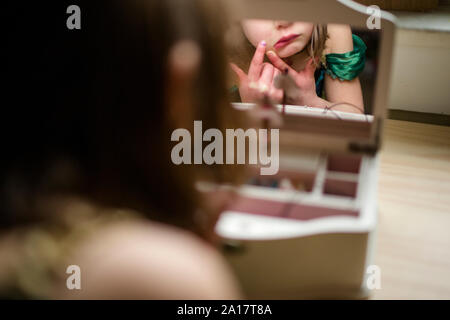 A little girl in princess costume stares at self in jewelry box mirror