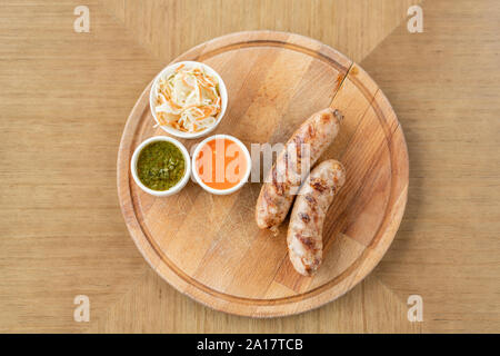 Grilled sausages. Serving on a wooden Board. Barbecue restaurant menu, a series of photos of different meats. Pickled cabbage and two sauces Stock Photo