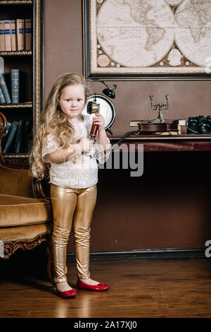 Little brooding child girl talking on a retro telephone in the room alone with sad emotions. Stock Photo