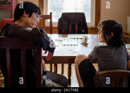 A father and son sit at table in morning light talking together Stock Photo