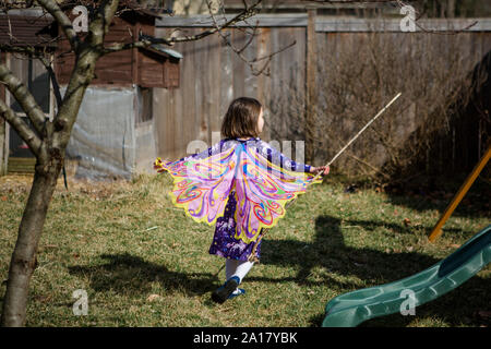 A happy child runs through a garden in Spring wearing butterfly wings Stock Photo