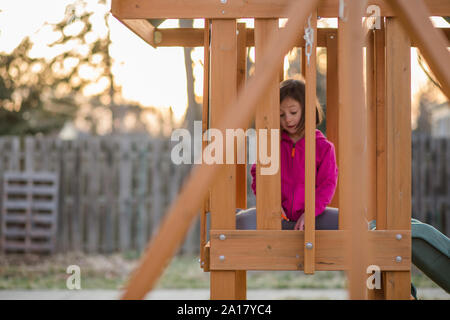 A small child sits on a swingset in backyard at sunset doing homework Stock Photo