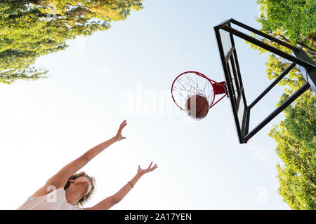 Winning throw. Low angle of a basketball player jumping while doing the winning throw Stock Photo