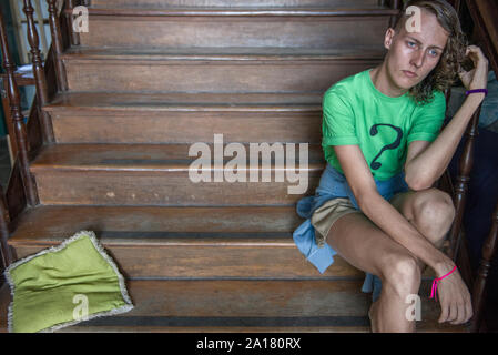 Young man seated on wood staircase wearing shirt with question mark Stock Photo