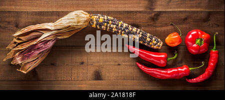 Dried multicolored corn cob with an assortment of fresh peppers on a dark wood background Stock Photo