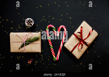 Christmas craft gift boxes with red ribbons, candies and red and golden decorations against black background. Stock Photo