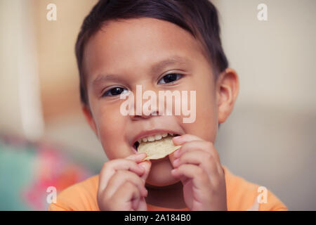 A cute young boy enjoying a unhealthy potato chip snack that he is holding to his mouth and is ready to bite. Stock Photo