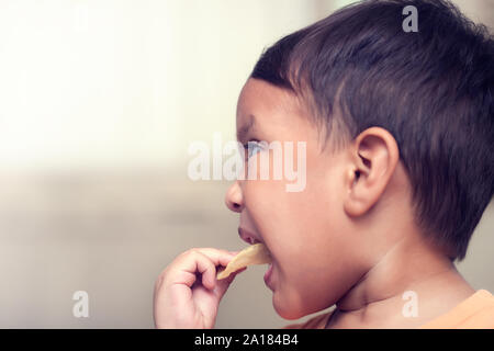 A kid forcibly putting a unhealthy potato chip snack in his mouth for eating while parents are away. Stock Photo
