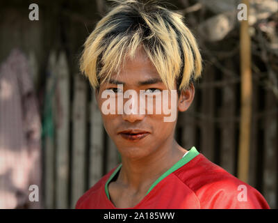 Young Burmese man with blonde-dyed hair and red, betel-stained lips chews a betel quid (betel leaf, areca nut, slaked lime, spices and tobacco). Stock Photo