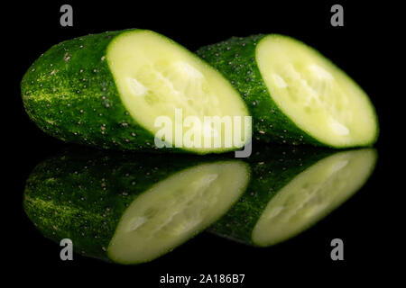 Group of two halves of fresh green pickling cucumber one halved isolated on black glass Stock Photo