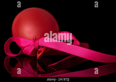 One whole red latex pastel ballon with pink ribbon isolated on black glass Stock Photo