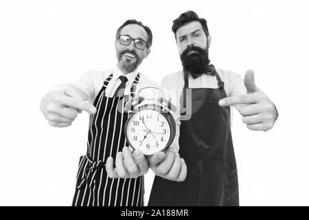 Time to cook. Men pointing at alarm clock. Man bearded hipster and mature chef apron white background. Cook dinner. We going to cook right now. Friends colleagues start cooking just on time. Stock Photo