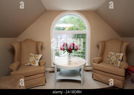 Flowers on round table with two seats in front of arched window Stock Photo