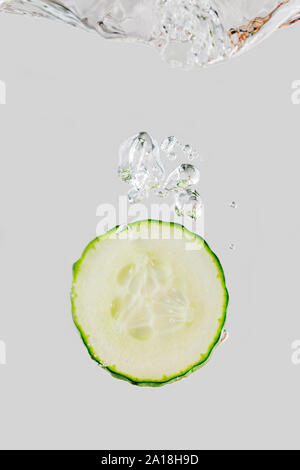 Lateral view of a dipping cucumber slice in water against gray background. Stock Photo