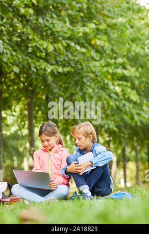 Girl using laptop computer together with her classmate while they sitting on green grass outdoors Stock Photo