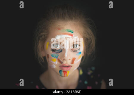 beautiful portrait of little caucasian girl face with colorful art painting on her with multicolor paint Stock Photo