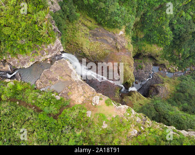 Aerial top view of travel couple waving to drone, standing on the edge of 500 feet waterfall in the tropical island jungle of Black river gorges Stock Photo